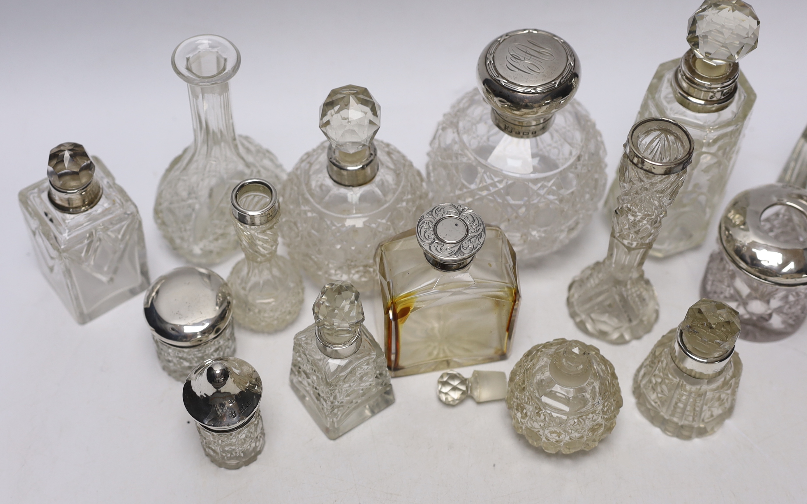 Fourteen assorted silver topped scent or toilet bottles and one without a mount, largest 14.7cm.